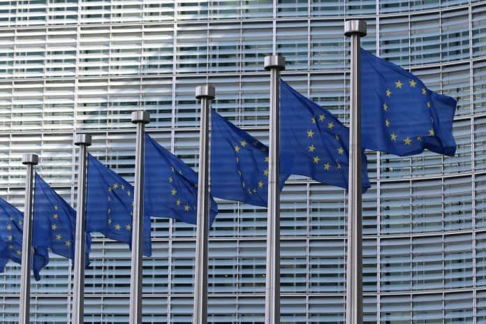 Fotografia de diversas Bandeiras da União Europeia, com um prédio ao fundo.