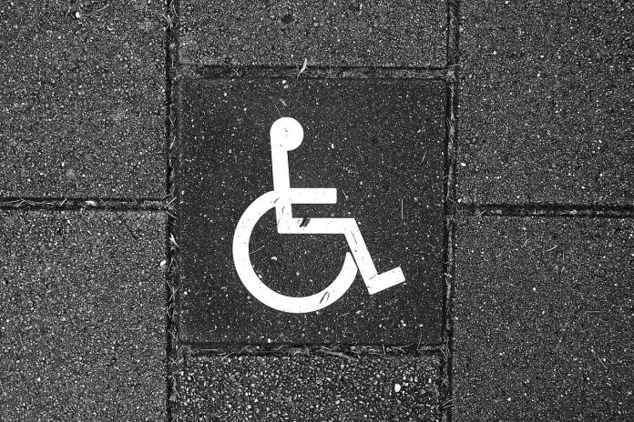 Fotografia do símbolo designado para deficientes físicos. O símbolo está pintado com tinta branca em uma superfície de concreto.