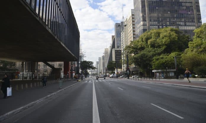 Foto da Avenida Paulista, em São Paulo, na altura do Masp, com a via com pouco movimento e enfatizando a calçada, o canteiro central e as árvores, com movimento de carros, motos e pedestres