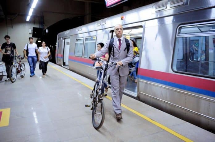 Fotografia de homem na plataforma saindo do vagão do metrô e com bicicleta, com mais usuário ao fundo e um deles também de bicicleta