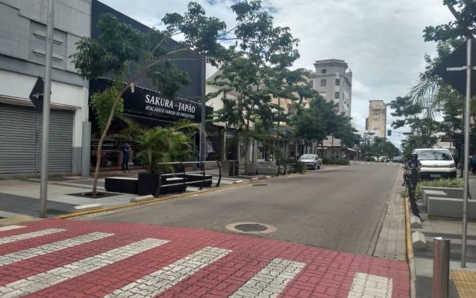 Fotografoa de avenida de comércio revitalizada, no centro de Campo Grande, com faixa acessível para pedestre, arborização, indivíduo de moto e veículos estacionados