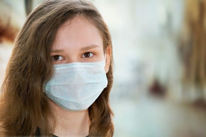 Fotografia de uma criança caucasiana de cabelos castanhos utilizando uma máscara de proteção ao coronavírus