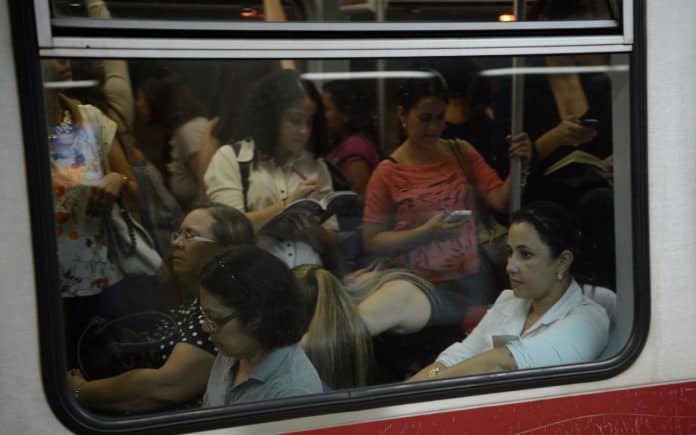 Fotografia de vagão de metrô ocupado por mulheres sentadas e em pé. Algumas mulheres estão lendo livros e outras acessando o celular