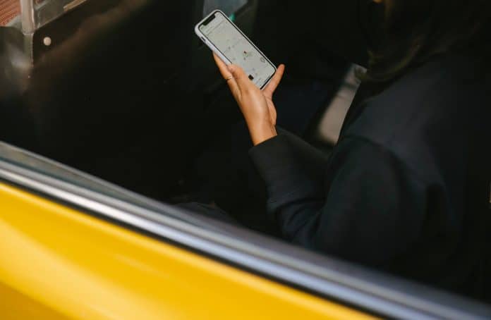 Fotografia de mulher sentando em veículo amarelo com o celular na mão, com ela olhando o mapa de aplicativo