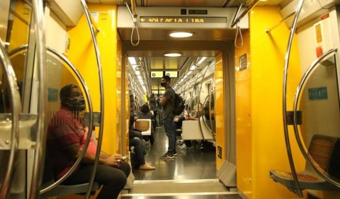 Fotografia da mobilidade urbana de vagão de metrô com passageiros em deslocamento. As pessoas usam máscara e estão sentadas e em pé