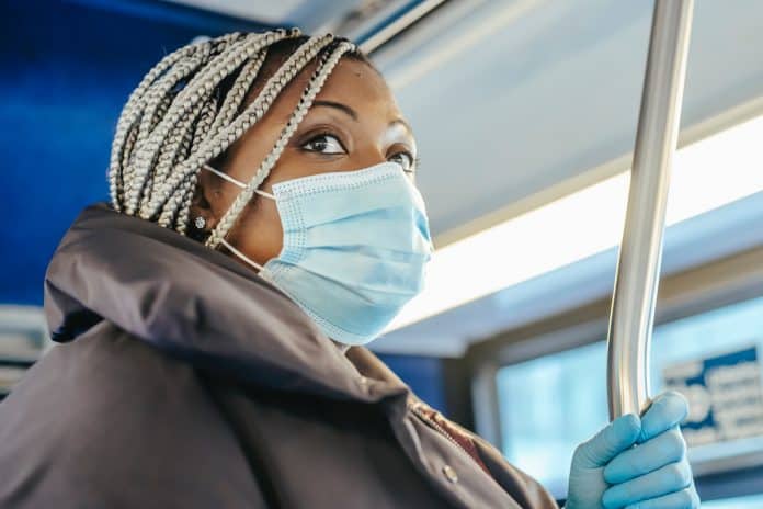 Fotografia de uma mulher negra em um ônibus utilizando máscara e luvas azuis como forma de proteção ao coronavírus