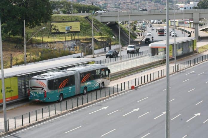 Fotografia de ônibus coletivo em avenida na cidade, com veículos na faixa também