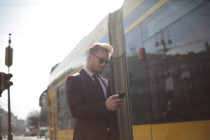 Fotografica de homem com celular ao lado de ônibus relacionando a mobilidade e universidades